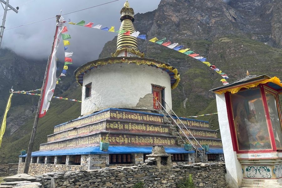 White Buddhist stupa with golden spire and colorful prayer flags against mountain backdrop